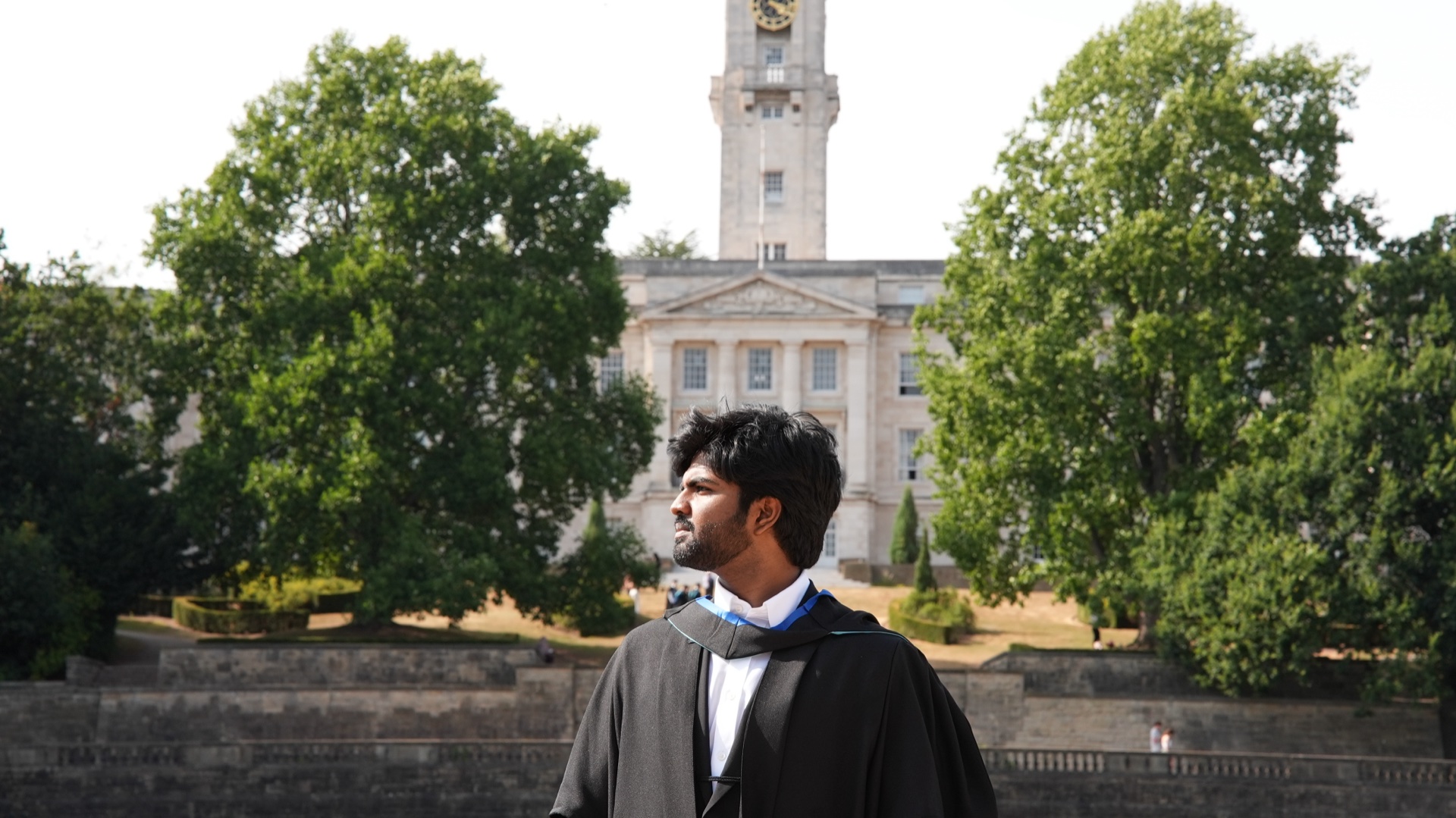 Full graduation photo — Veerendhra Kumar in front of the university clock tower
