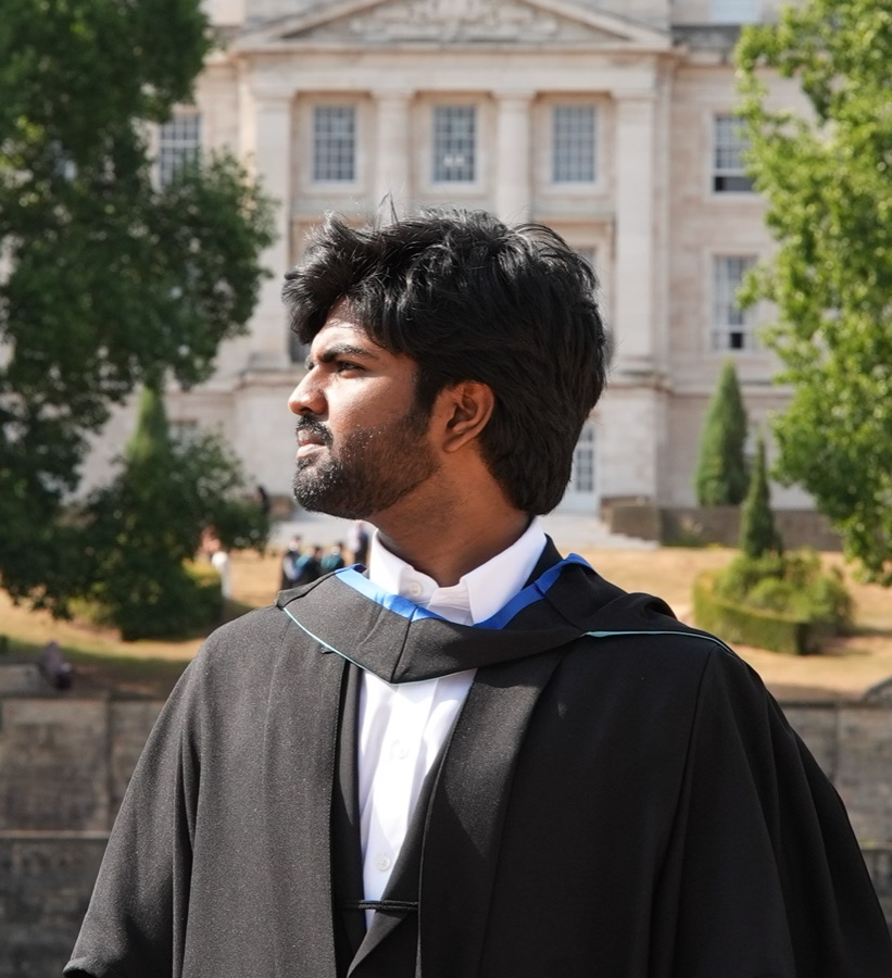 Veerendhra Kumar in a graduation gown in front of a university clock tower